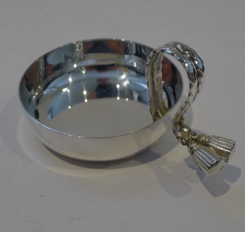 fig 1. A circular silver-plated shallow dish with a polished reflective finish, featuring an arched twisted handle terminating in decorative double tassels.