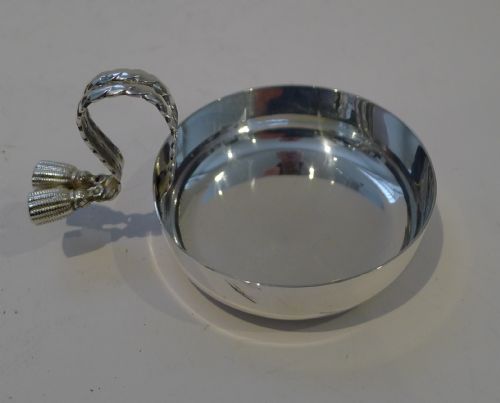 fig 2. A circular silver-plated shallow dish with a polished reflective finish, featuring an arched twisted handle terminating in decorative double tassels.
