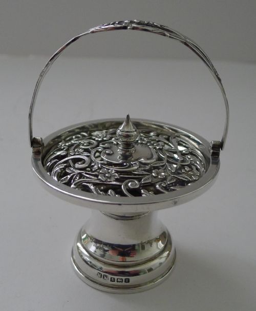 fig 1. An Edwardian sterling silver pedestal pot pourri basket featuring an overhead swing handle and a pierced floral scrollwork lid topped with a pointed finial.