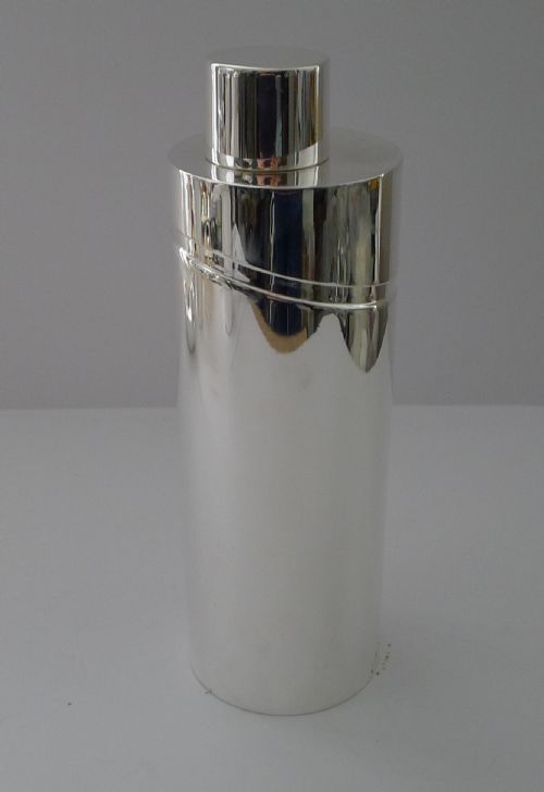 fig 3. A sleek, highly polished cylindrical silver-plated cocktail shaker with an angled upper seam and fitted cylindrical cap.