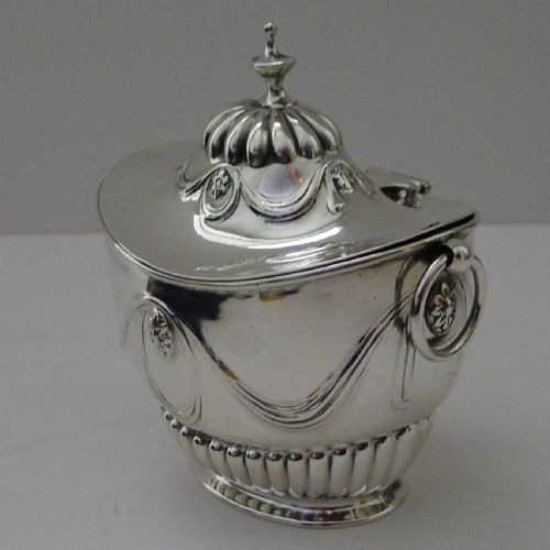 fig 1. An antique Edwardian sterling silver tea caddy featuring lower fluted detailing, embossed swag motifs, drop ring handles, and a finial lid.