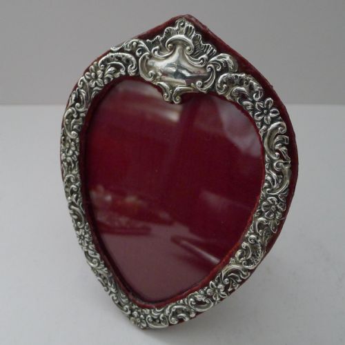 fig 1. An Edwardian heart-shaped sterling silver photo frame with ornate scroll and floral repousse work set against a crimson velvet backing.