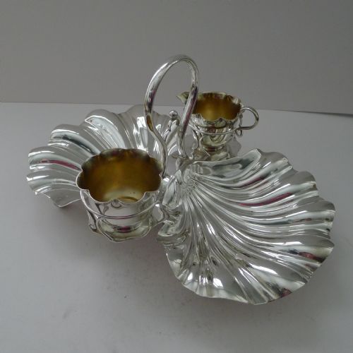fig 1. An antique silver-plated strawberry set featuring two fluted shell-shaped serving dishes, a central overhead loop handle, and two small gilt-lined pots.