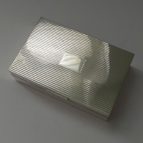fig 1. A rectangular sterling silver cigarette box with an engine-turned reeded pattern on the lid and a plain central rectangular cartouche.