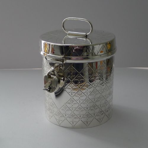 fig 2. A cylindrical silver-plated Victorian biscuit box featuring engraved geometric trellis patterning, a loop top handle, and a hinged clasp with a padlock.