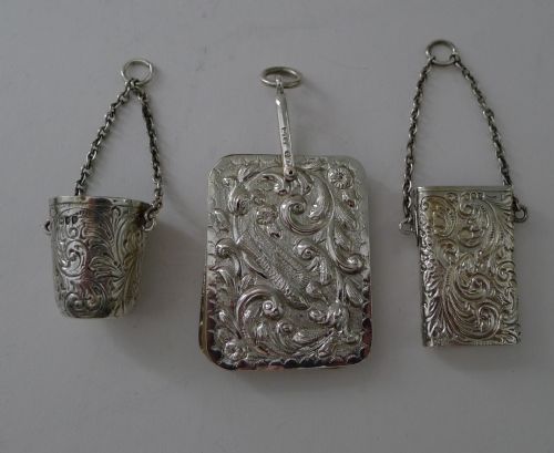 fig 2. A Victorian sterling silver chatelaine featuring an ornate pierced scroll waist clip suspending five linked chains attached to silver accessories including a scent bottle, card case, pencil, and thimble holder.