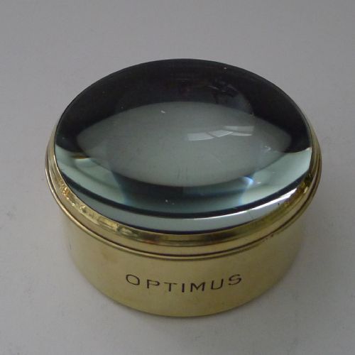fig 1. A cylindrical brass-bound magnifying glass paperweight engraved with the name Optimus around its base.