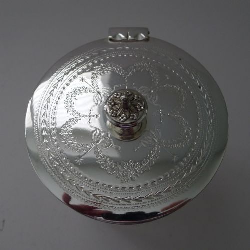 fig 1. An Edwardian silver-plated and etched glass cylindrical biscuit box featuring floral ribbon motifs, an engraved lid with a central finial, and an integrated footed tray base.