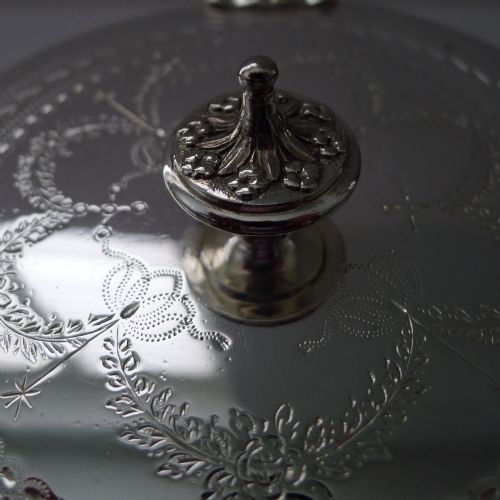 fig 2. An Edwardian silver-plated and etched glass cylindrical biscuit box featuring floral ribbon motifs, an engraved lid with a central finial, and an integrated footed tray base.