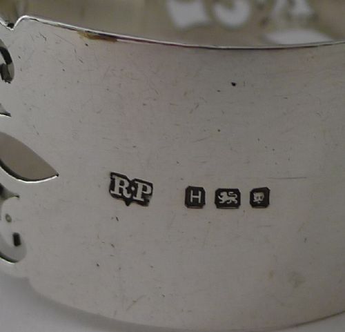 A cylindrical sterling silver napkin ring featuring openwork scroll patterns and an unengraved shield cartouche. View V