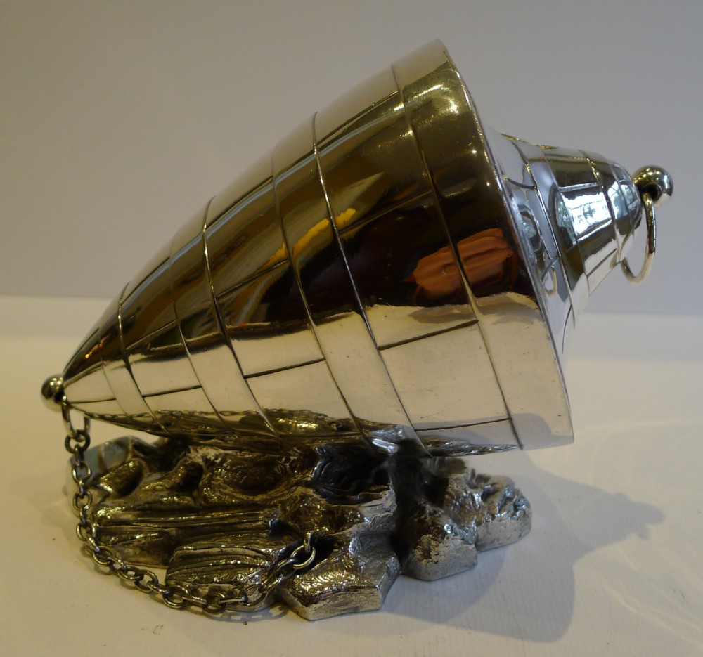 A silver-plated Victorian spoon warmer shaped like a conical marine buoy resting on a cast metal rocky base with an attached chain.