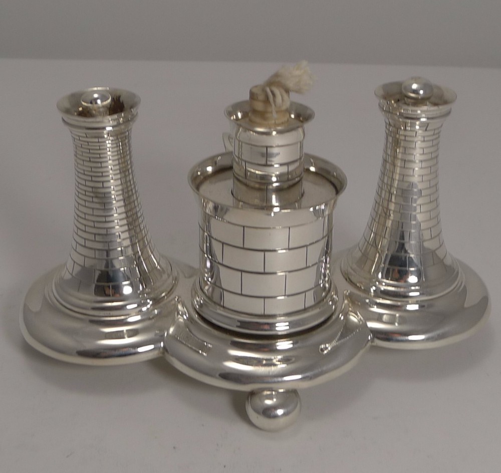A silver-plated novelty table lighter featuring three brick-patterned cylindrical towers mounted on a moulded tri-form base with small ball feet.