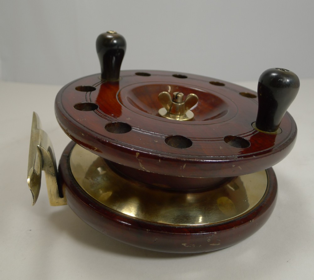 An antique mahogany circular fishing reel featuring brass fittings, twin handles, and a brass mounting foot. View II