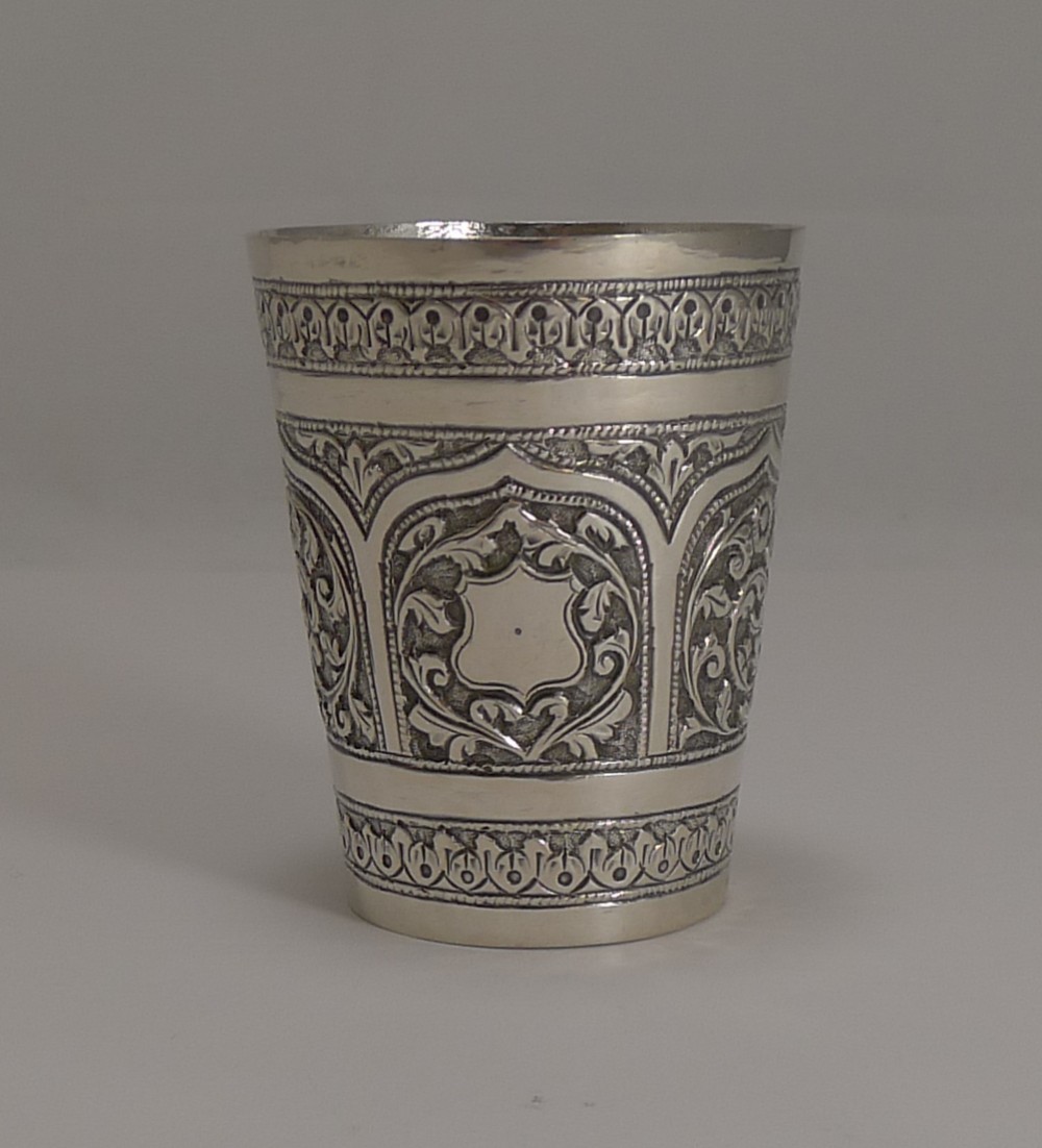 An antique Anglo-Indian sterling silver beaker featuring raised repousse floral motifs and decorative arch borders.