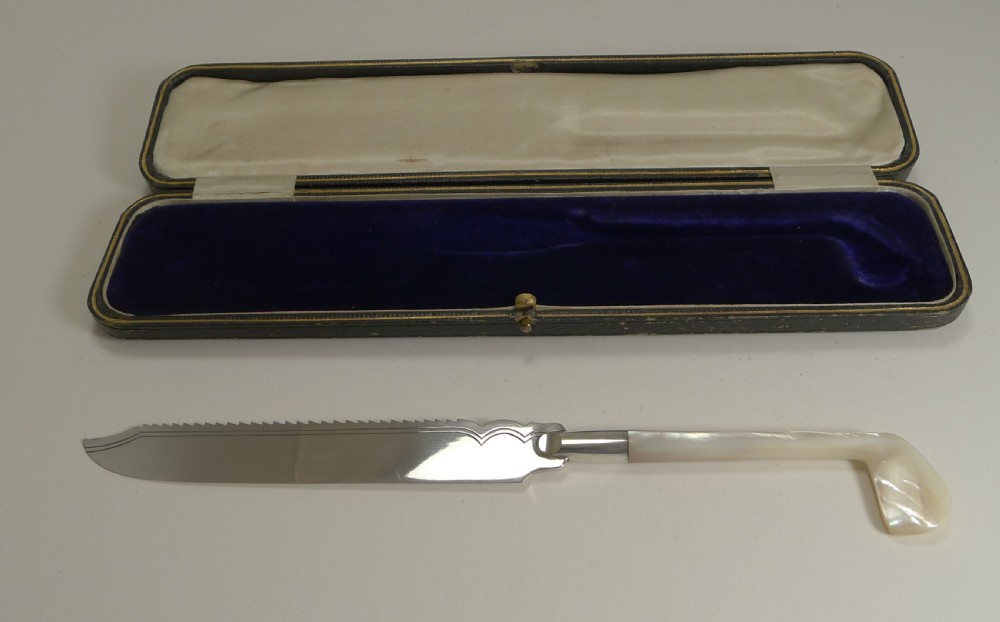 An Edwardian silver-plated cake knife with a serrated edge and a mother of pearl handle shaped like a golf club, displayed inside its fitted velvet presentation case. View III