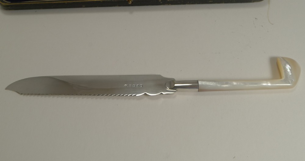 An Edwardian silver-plated cake knife with a serrated edge and a mother of pearl handle shaped like a golf club, displayed inside its fitted velvet presentation case. View IV