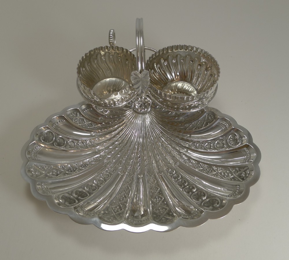 A silver-plated strawberry set featuring a scalloped shell tray with two attached fluted bowls and a central arched handle.