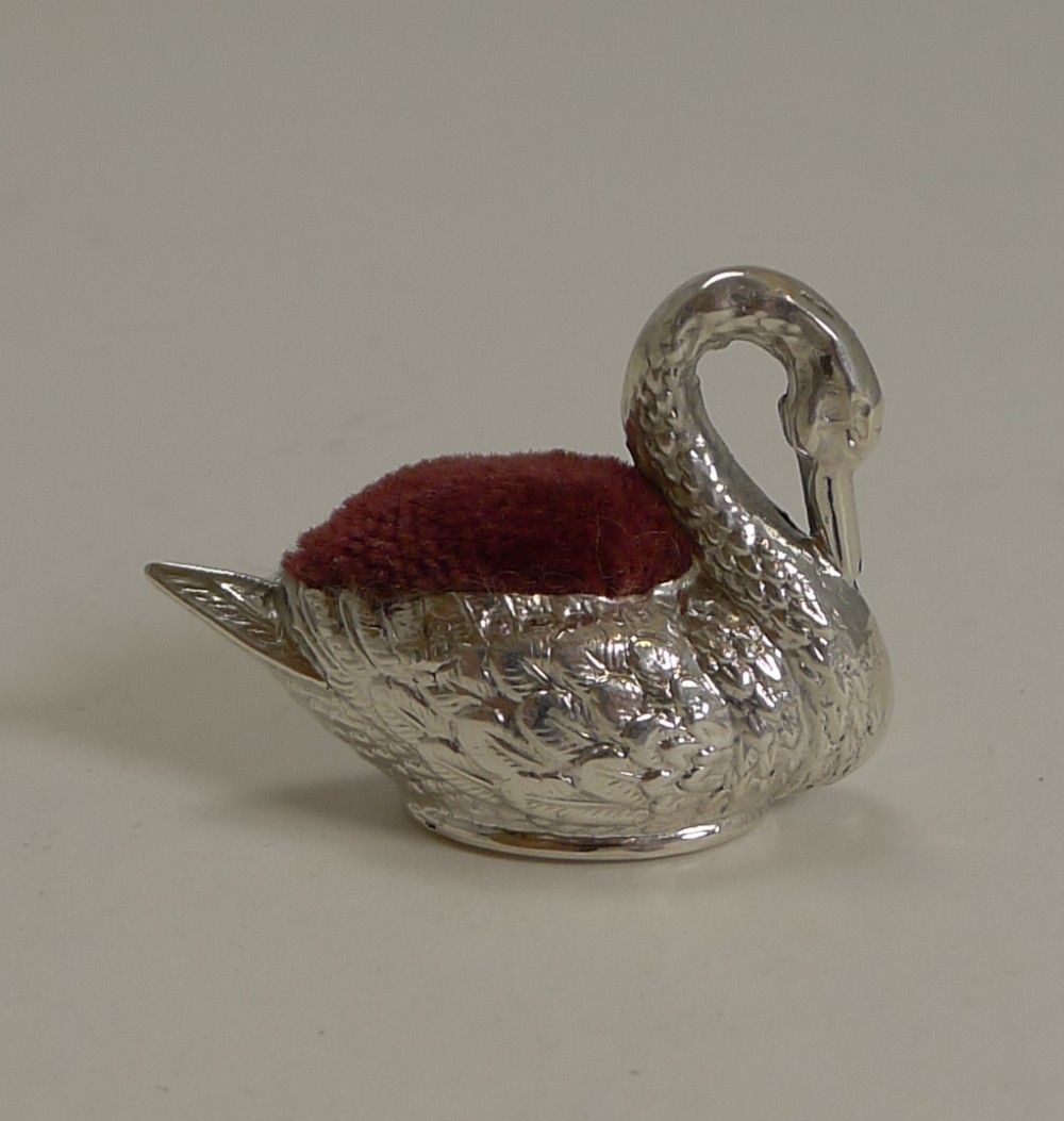 A miniature Edwardian sterling silver pin cushion cast in the shape of a swan with a maroon velvet insert.