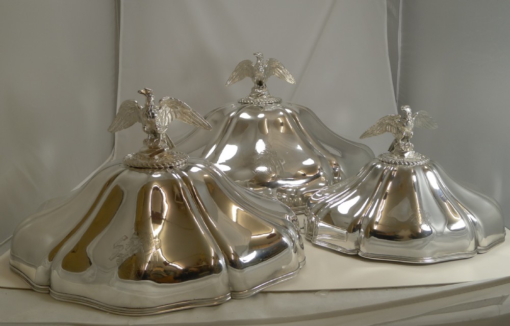 A set of three graduated silver meat domes with lobed bodies and detailed eagle finials.