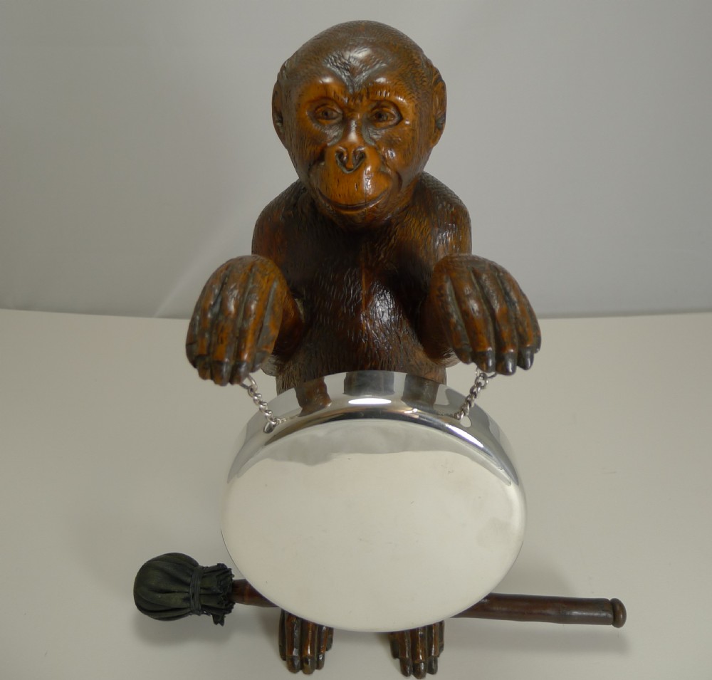 A late 19th-century hand-carved wooden monkey figure holding a suspended round silver-coloured metal dinner gong with an accompanying padded striker.