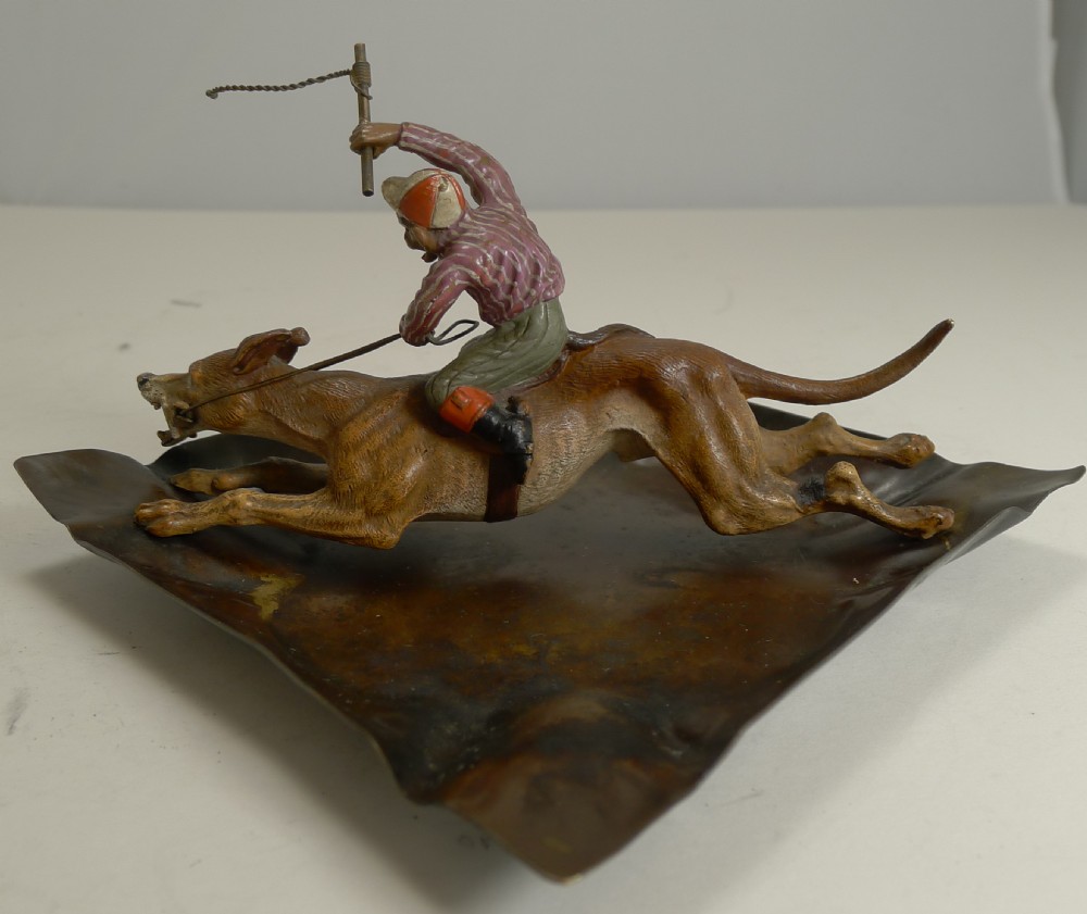 A cold-painted Vienna bronze dish depicting a monkey holding a whip while riding a racing greyhound mounted on a wavy metal base. View III