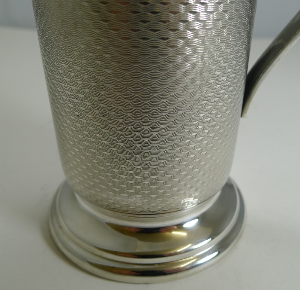 An Art Deco silver-plated cocktail mixer featuring an engine-turned textured body, a curved side handle, a pouring spout, and a lid topped with a spherical finial. View VIII