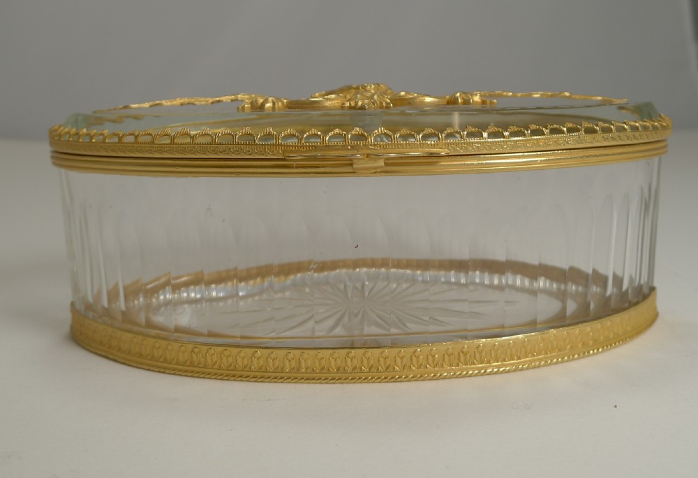 An oval cut crystal box featuring a hinged lid decorated with a detailed gilt metal spread-eagle mount. View XII