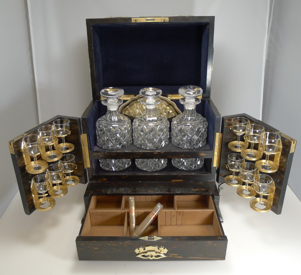 An antique dark coromandel wood decanter box embellished with decorative pierced brass straps and stone mounts, set alongside three cut crystal decanters and a silvered tray with glasses. View VII