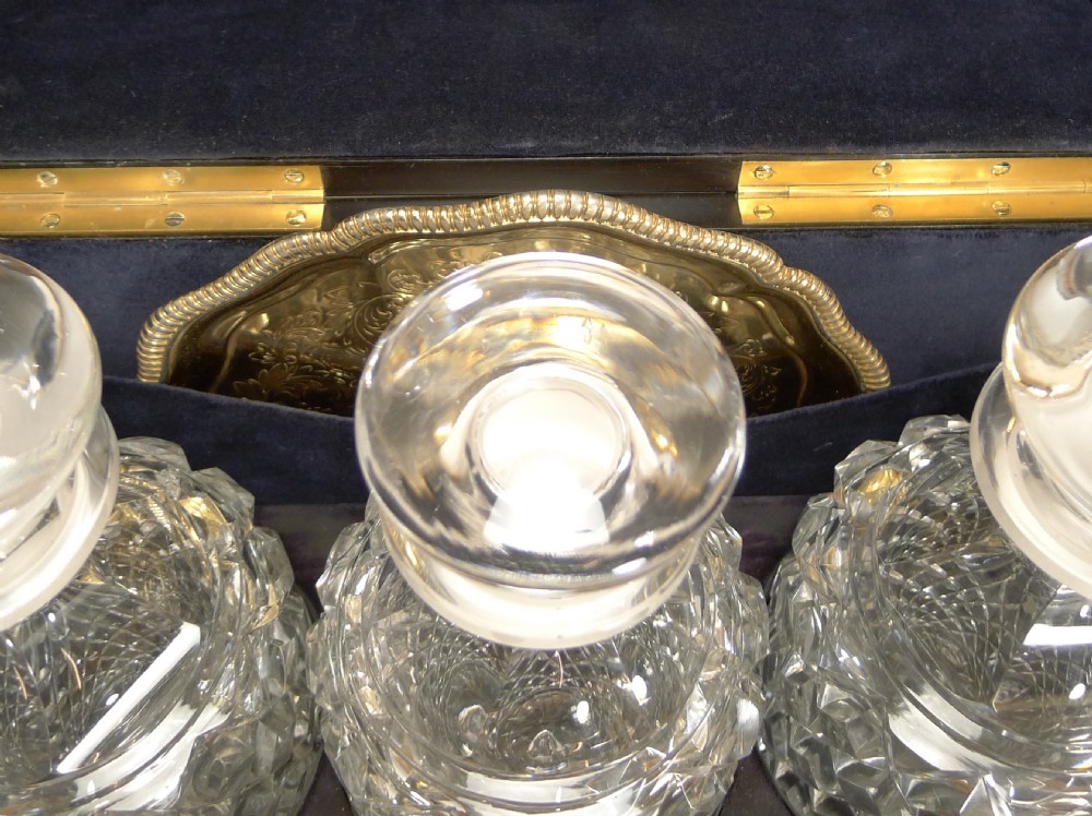 An antique dark coromandel wood decanter box embellished with decorative pierced brass straps and stone mounts, set alongside three cut crystal decanters and a silvered tray with glasses. View VIII