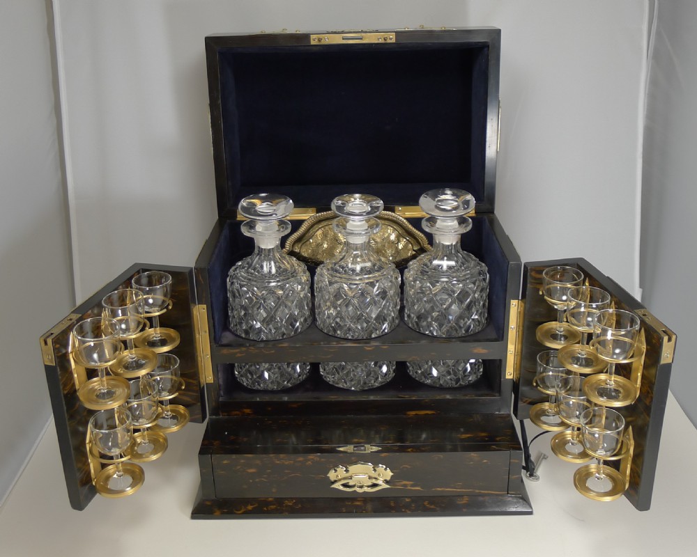 An antique dark coromandel wood decanter box embellished with decorative pierced brass straps and stone mounts, set alongside three cut crystal decanters and a silvered tray with glasses. View XIV