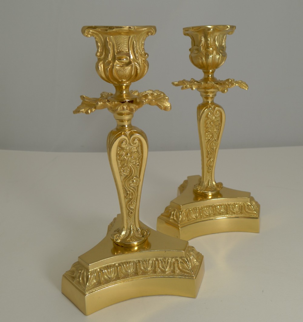 A pair of late 19th-century French gilded bronze candlesticks featuring ornate floral scroll stems and flared triform bases.
