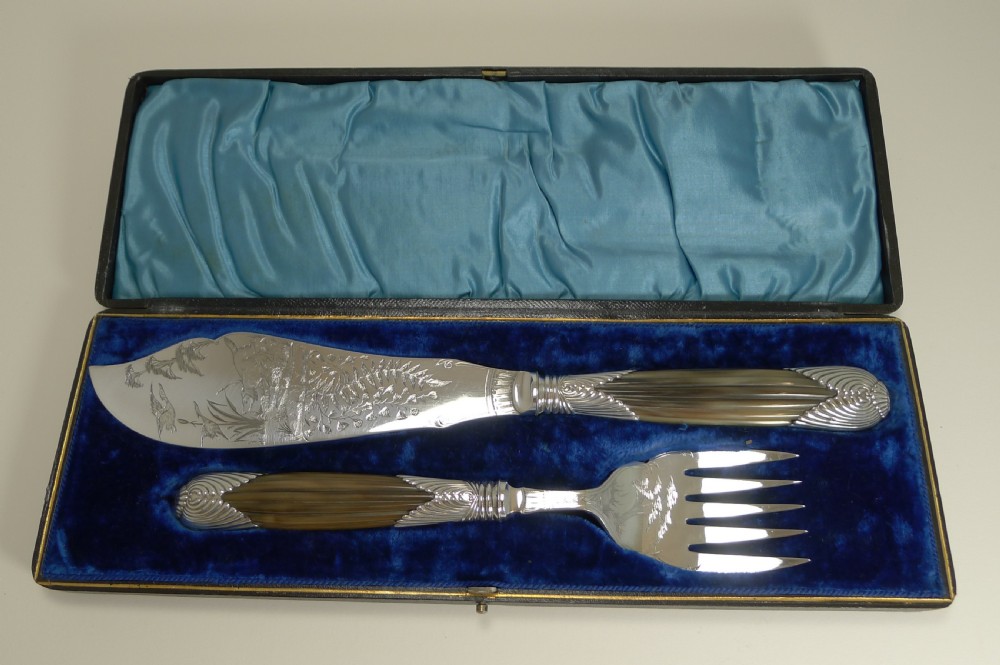A cased pair of late Victorian fish servers featuring engraved silver-plated blades with hunting dog motifs and fluted horn handles.