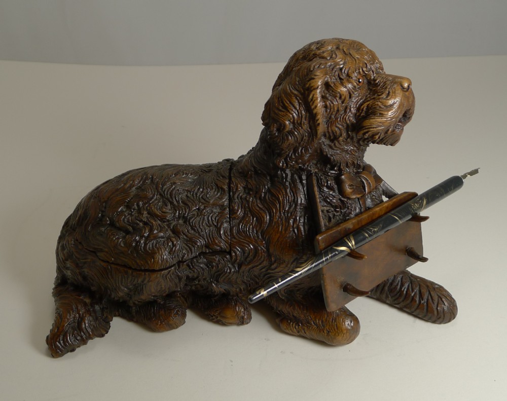 A nineteenth-century dark brown hand-carved wooden inkwell and pen rest sculpted in the form of a recumbent dog holding a pen rack in its front paws.