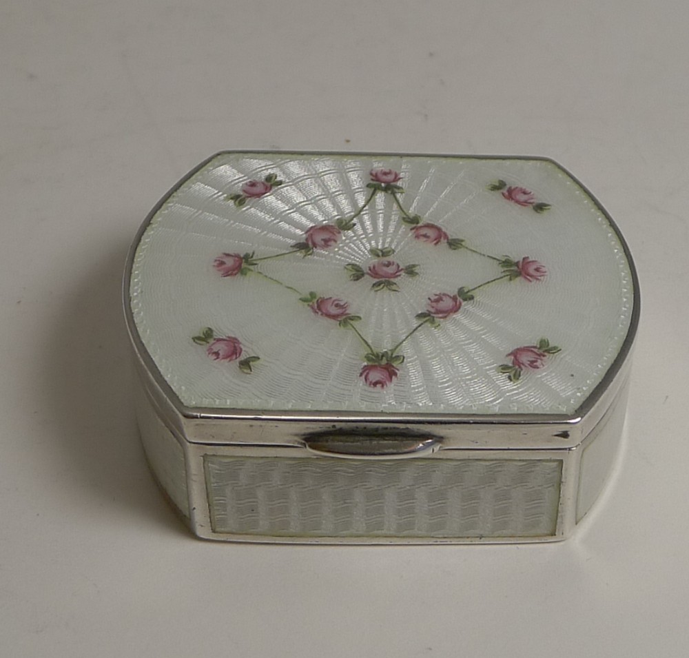 An octagonal sterling silver pill box with a white guilloche enamel lid decorated with engine-turned sunburst patterns and hand-painted pink rose garlands.