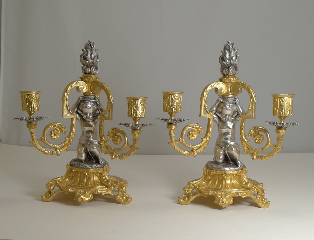 A pair of French gilt and silvered bronze three-branch candelabra featuring kneeling cherubs and central flame finials.