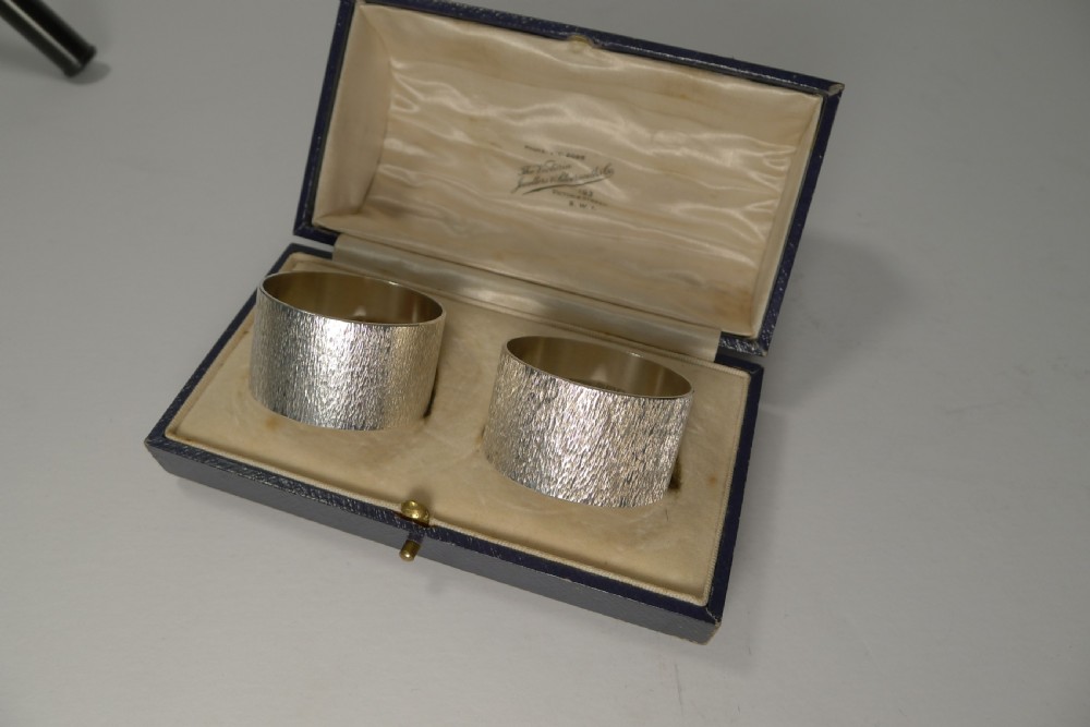 A pair of textured sterling silver napkin rings displayed inside an open dark blue fitted presentation box lined with cream silk.