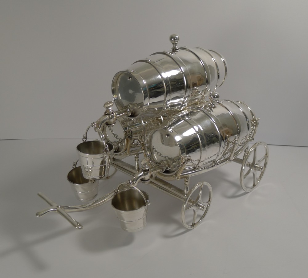 A Victorian silver-plated novelty spirit set featuring three miniature barrels mounted on a four-wheeled cart with hanging bucket cups.
