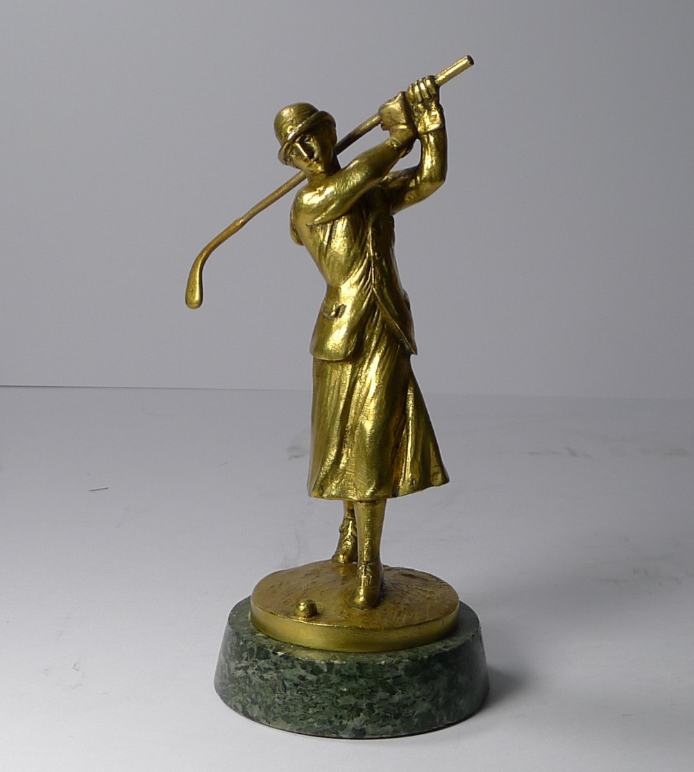 A gilt bronze Art Deco sculpture depicting a lady golfer mid-swing mounted on a circular green marble base.