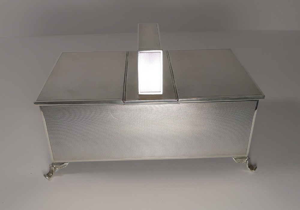 A rectangular Art Deco sterling silver cigarette box featuring engine-turned geometric patterning, a central angled handle, and four corner feet. View VII