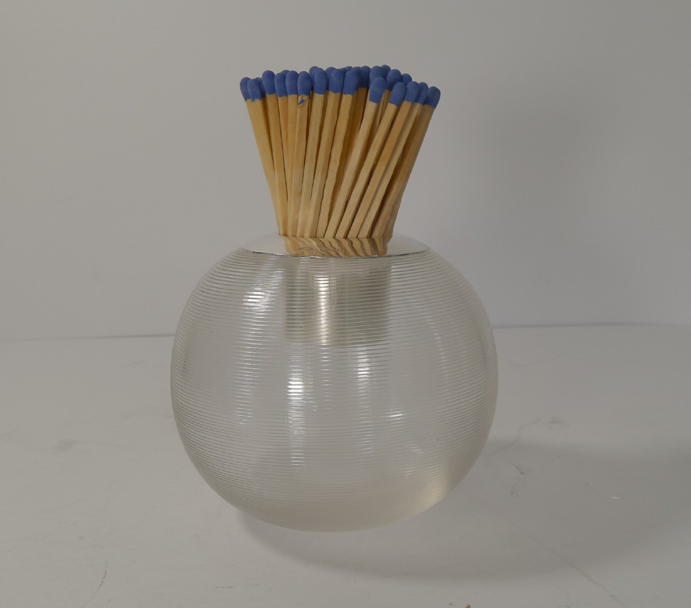 A spherical clear glass match striker featuring fine horizontal threaded ridges and a sterling silver collar holding wooden matches.