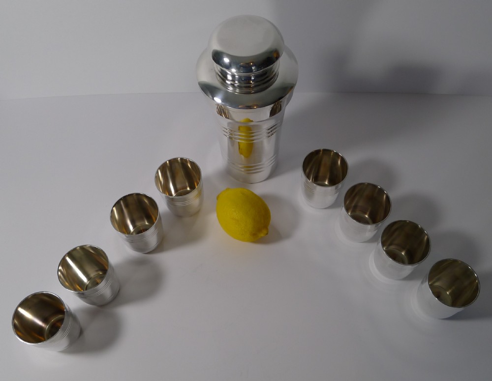 A silver-plated Art Deco cocktail shaker and eight matching cups housed within an open burgundy velvet and cream satin fitted case. View IX