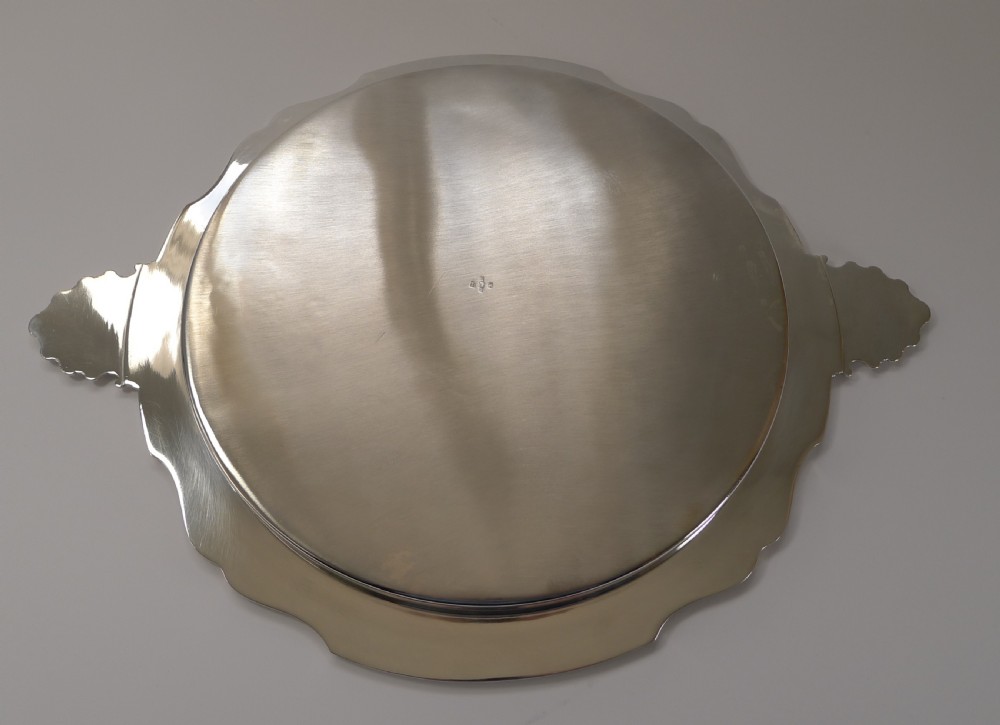 A circular silver-plated serving tray featuring a polished surface, scalloped moulded border, and shell-form handles. View XI