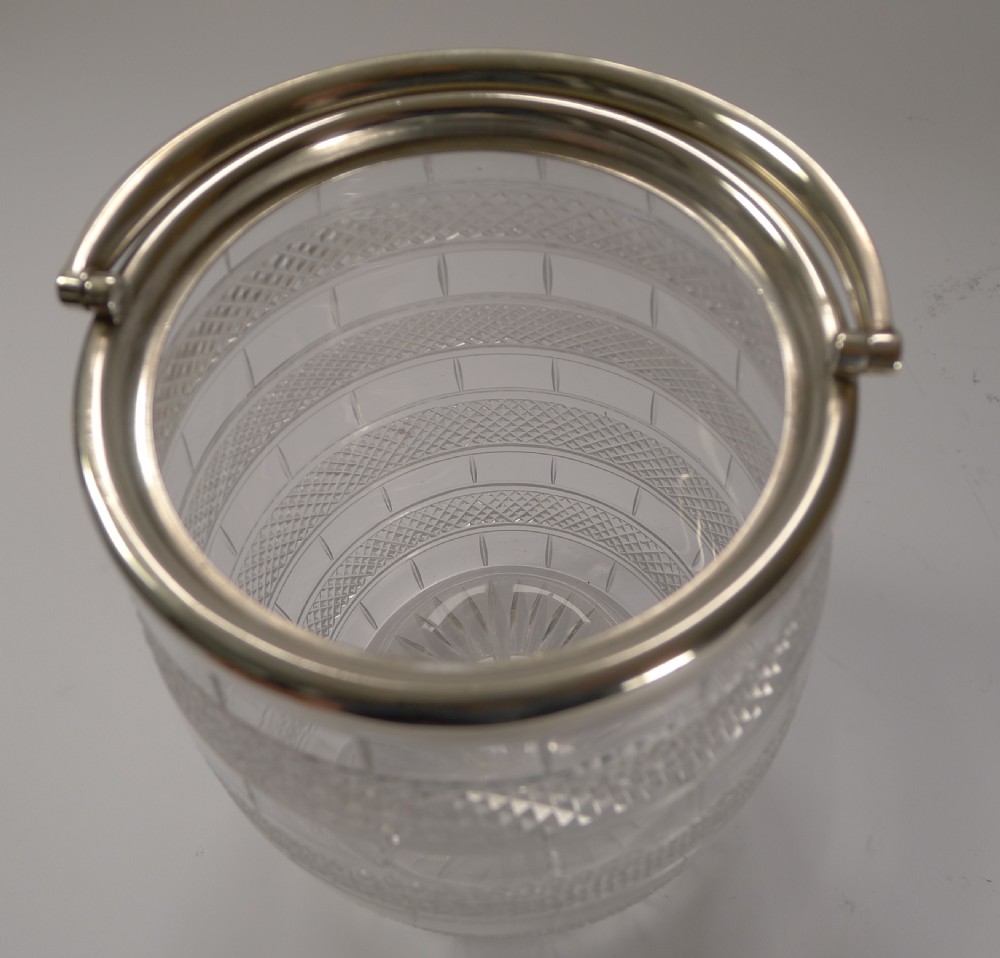 An English Victorian barrel-shaped cut glass biscuit container featuring geometric panel patterns, a silver-plated rim, a swing handle, and a fitted lid with a finial. View IV