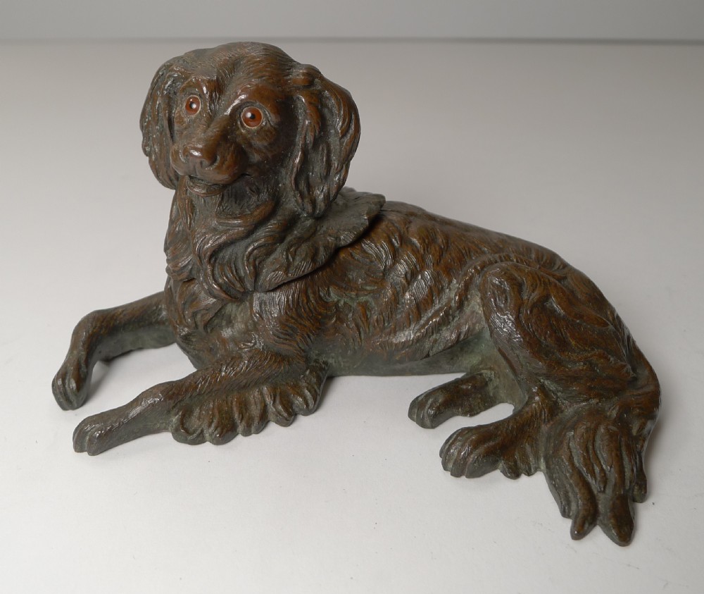 A nineteenth-century cast bronze inkwell modelled as a reclining King Charles Spaniel with glass eyes and detailed fur texturing.