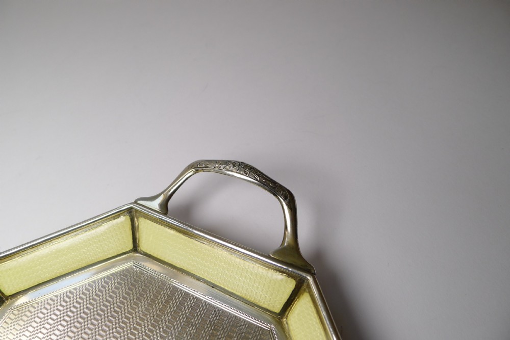 An octagonal sterling silver tray featuring a central engine-turned pattern, a cream guilloche enamel border, and integrated side handles. View VI
