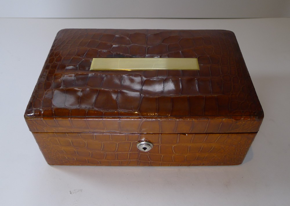 A rectangular warm brown crocodile skin jewellery box featuring a brass plaque on the lid and a lock with a key. View III