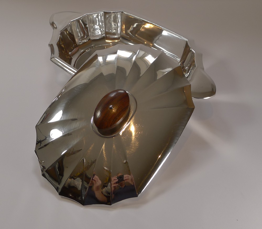 An Art Deco silver-plated covered serving dish featuring a faceted fluted body, matching lid, and a dark wood oval finial.