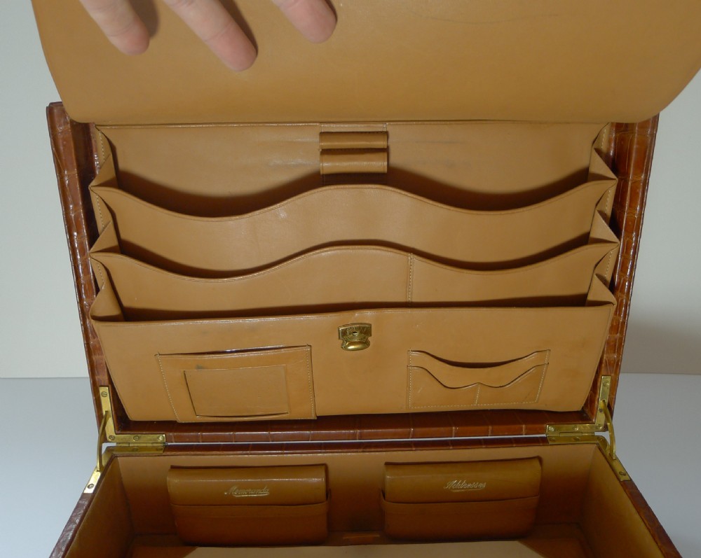 A tan crocodile hide writing case with double brass locks, displayed with a matching leather blotter pad and small notebooks. View VIII