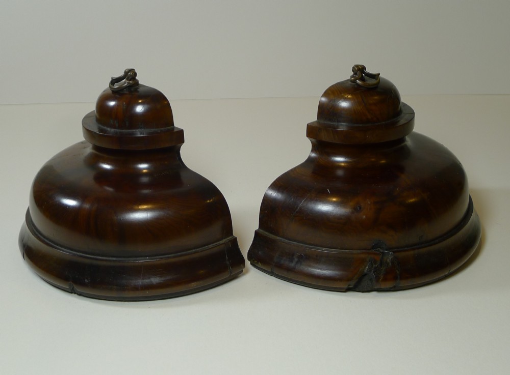 A pair of turned dark yew wood bookends featuring stepped moulded bases, domed tops, and brass ring handles.