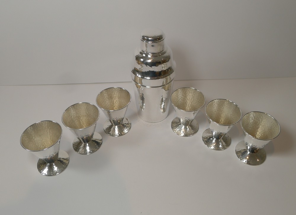 An Art Deco silver-plated cocktail shaker set with a hammered texture, featuring a central shaker flanked by six matching flared goblets. View II